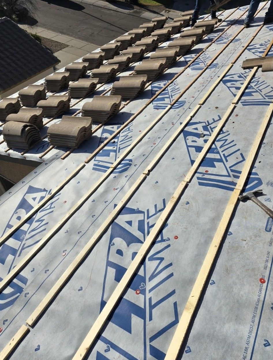 Roof under construction with blue waterproofing membrane and rows of roof tiles.