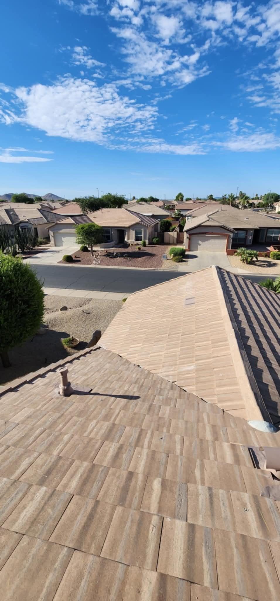 Rooftop view of a suburban neighborhood under a bright blue sky with scattered clouds.