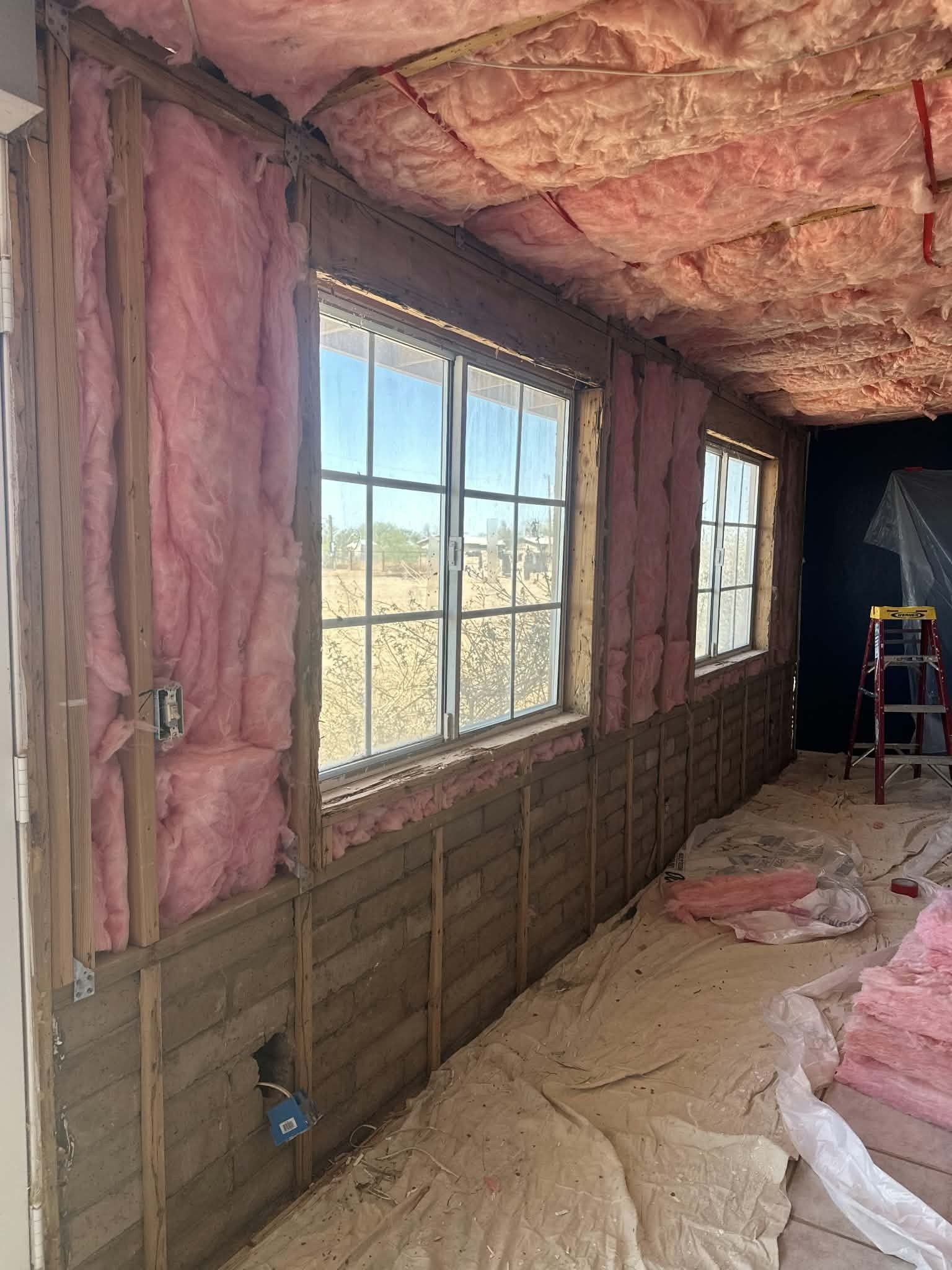 Insulated interior wall with two windows, exposed framing, and construction ladder in a room under renovation