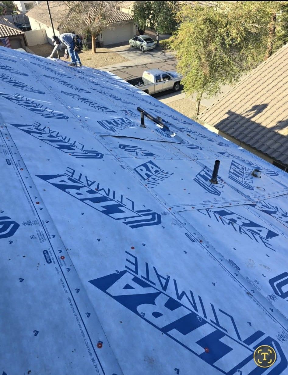 Roof under construction with blue underlayment and workers in the background