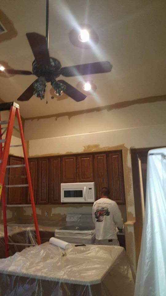 Kitchen under renovation with ceiling fan, ladder, cabinets, and a person working at the counter