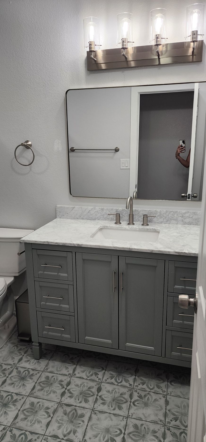 Modern bathroom vanity with marble countertop, mirror cabinet, wall sconces, and patterned tile floor.