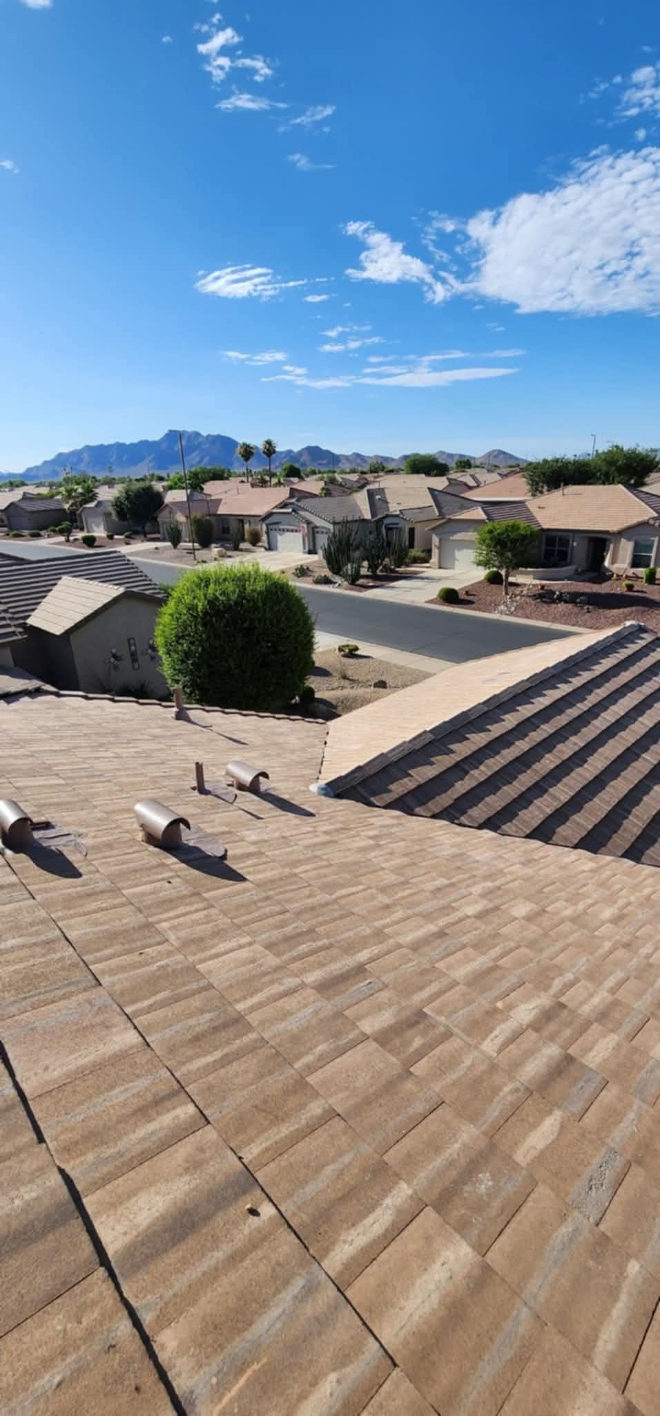 Rooftops of a suburban neighborhood under a bright blue sky with distant mountains