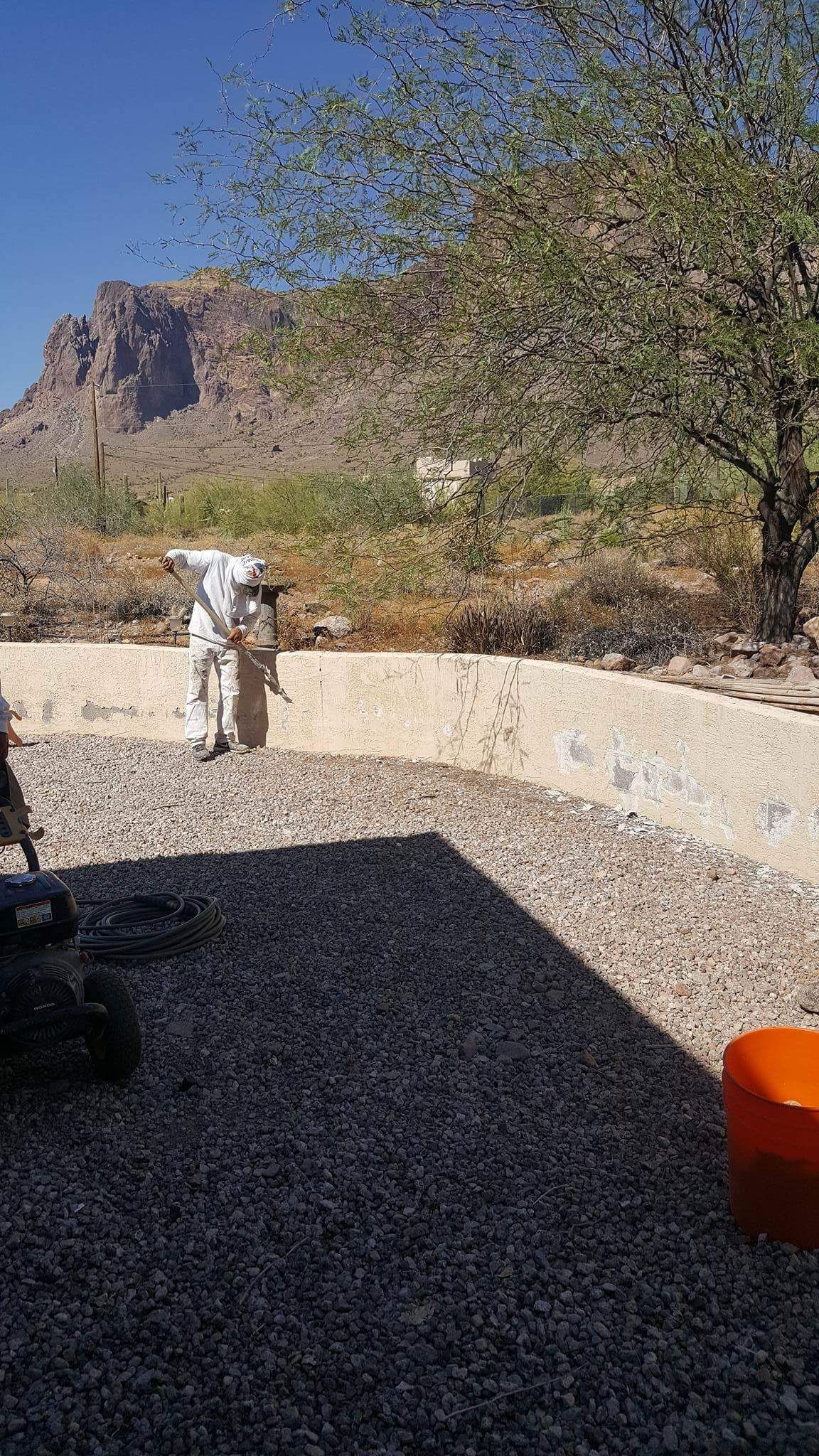 Person standing on a gravel patio with a stone wall, desert trees, and mountains in the background.