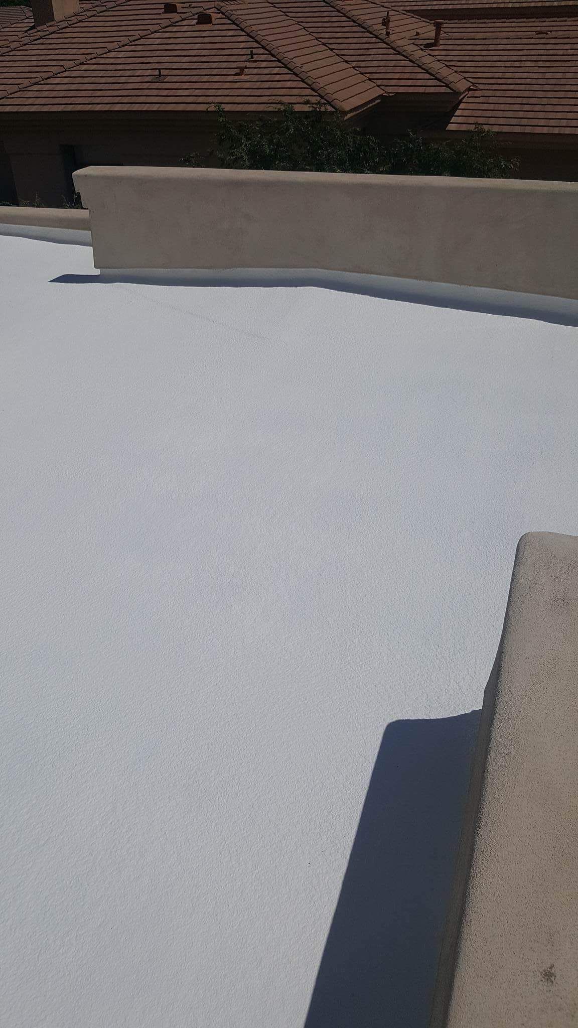White rooftop with a low beige wall and red-tiled roof in the background.