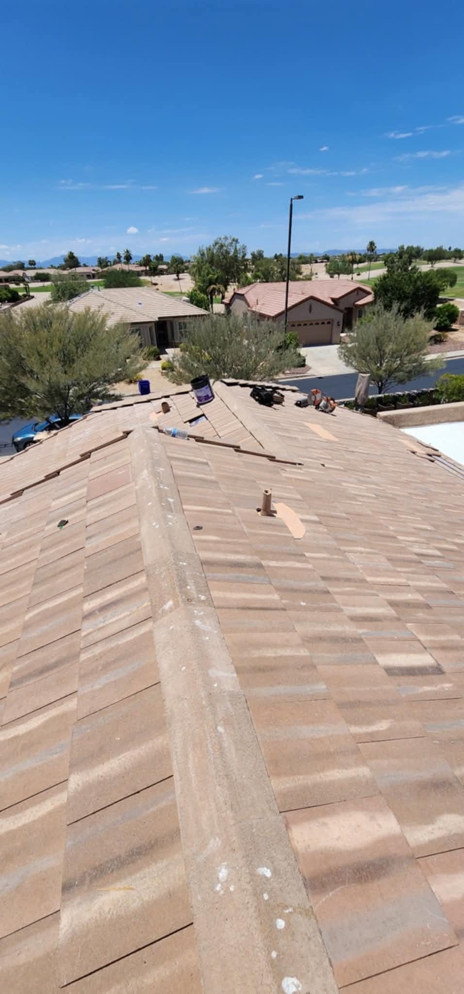 Rooftop view over tan shingles toward neighboring houses and a clear blue sky