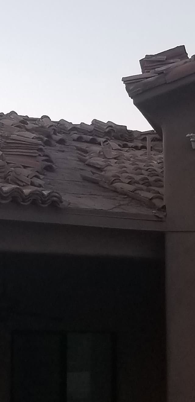 Damaged tiled roof with debris on a house under a gray sky