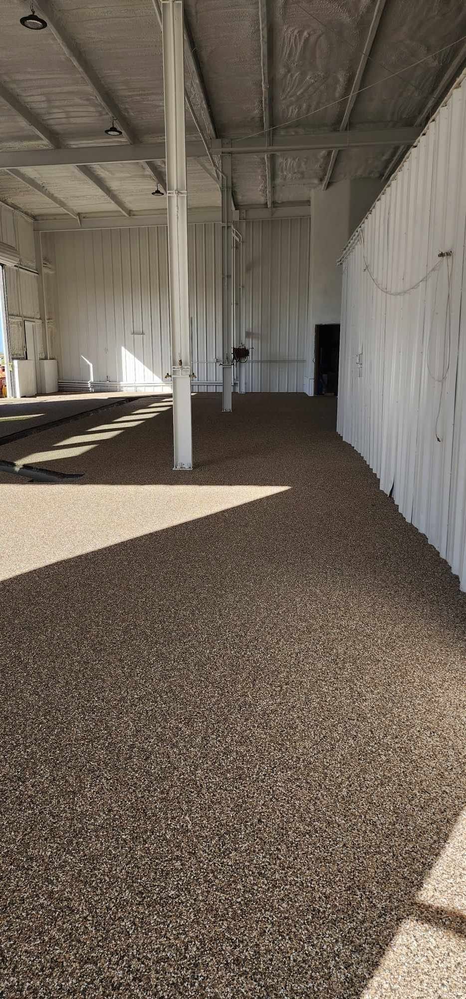 Empty industrial interior with white columns, corrugated walls, and gravel-covered floor near an open doorway