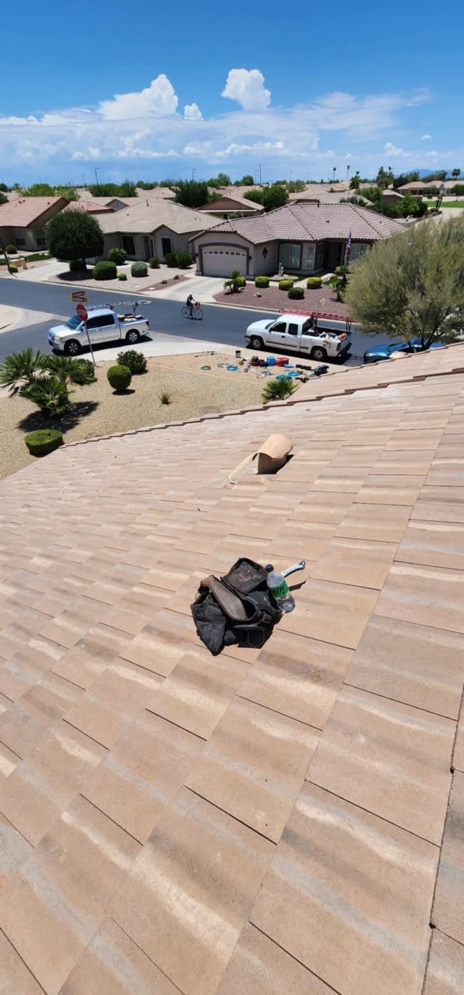 Roof shingles with a small object in the foreground, overlooking a suburban neighborhood under a blue sky