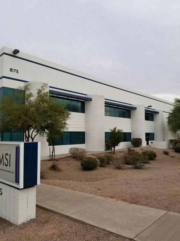 Modern office building with white facade, blue accents, landscaping, and an MSI sign by the sidewalk