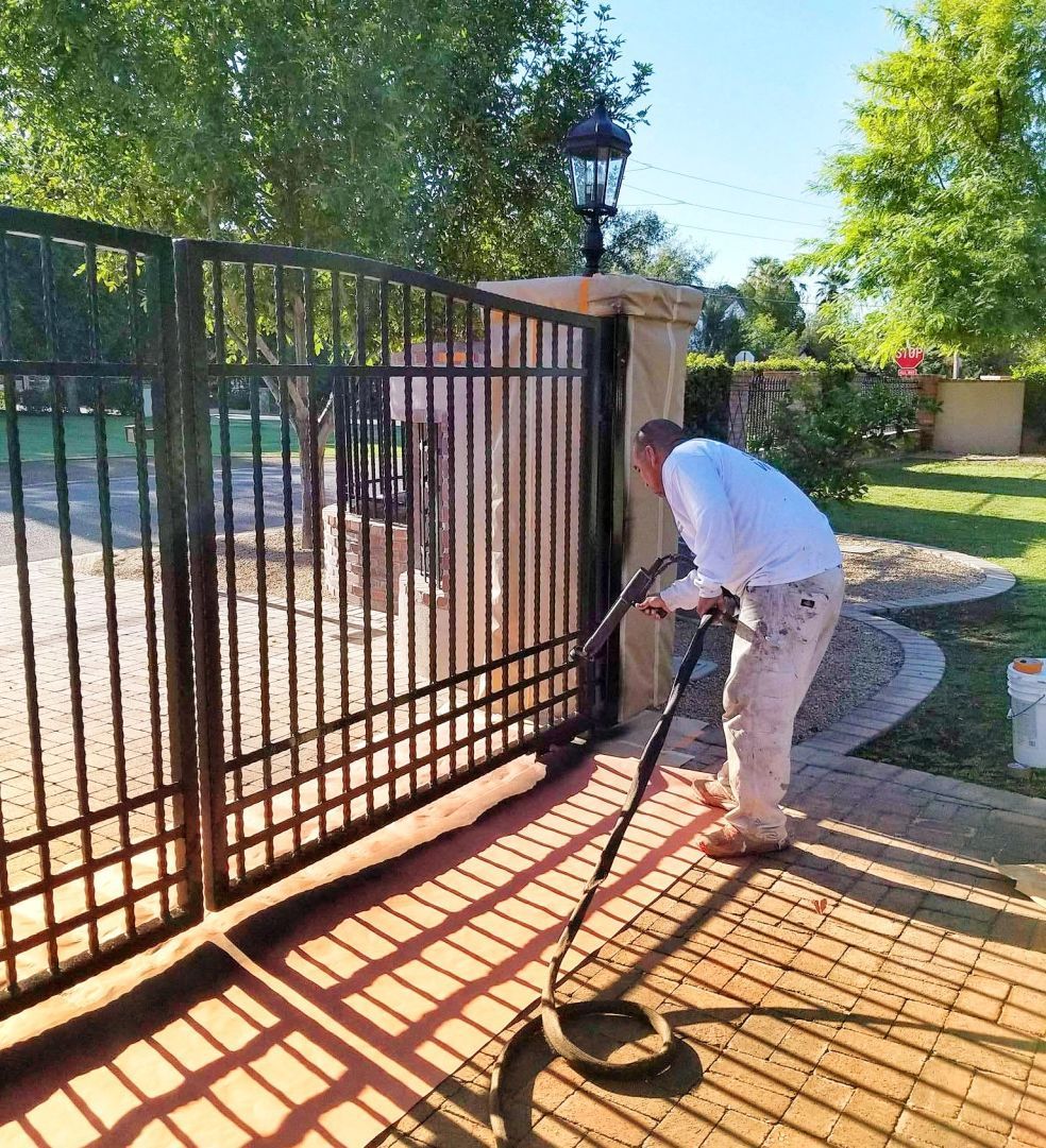 Person pressure-washing a black metal gate on a sunny patio.