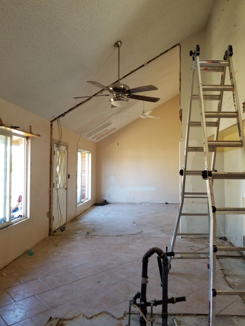 Interior under renovation with ladder, ceiling fan, and exposed ceiling in a long room