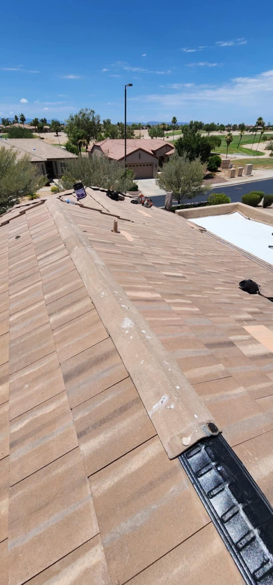 Rooftop view of tan shingles with solar panels, overlooking a suburban neighborhood under a blue sky