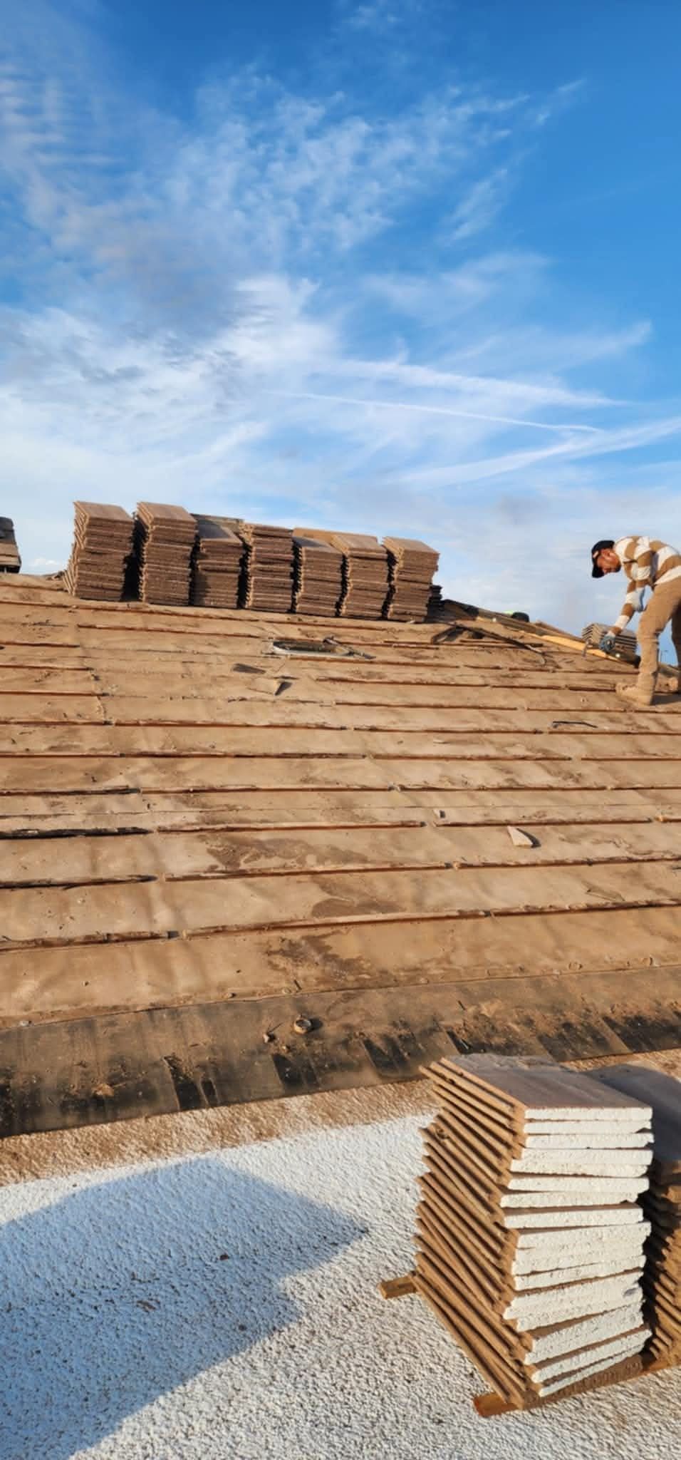 Stacked bricks on a construction site under a blue sky, with gravel and a partially built wall.