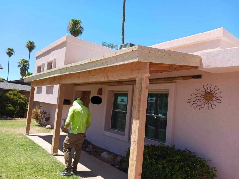 Person walking under a patio beside a pink house with windows and sun wall decor.