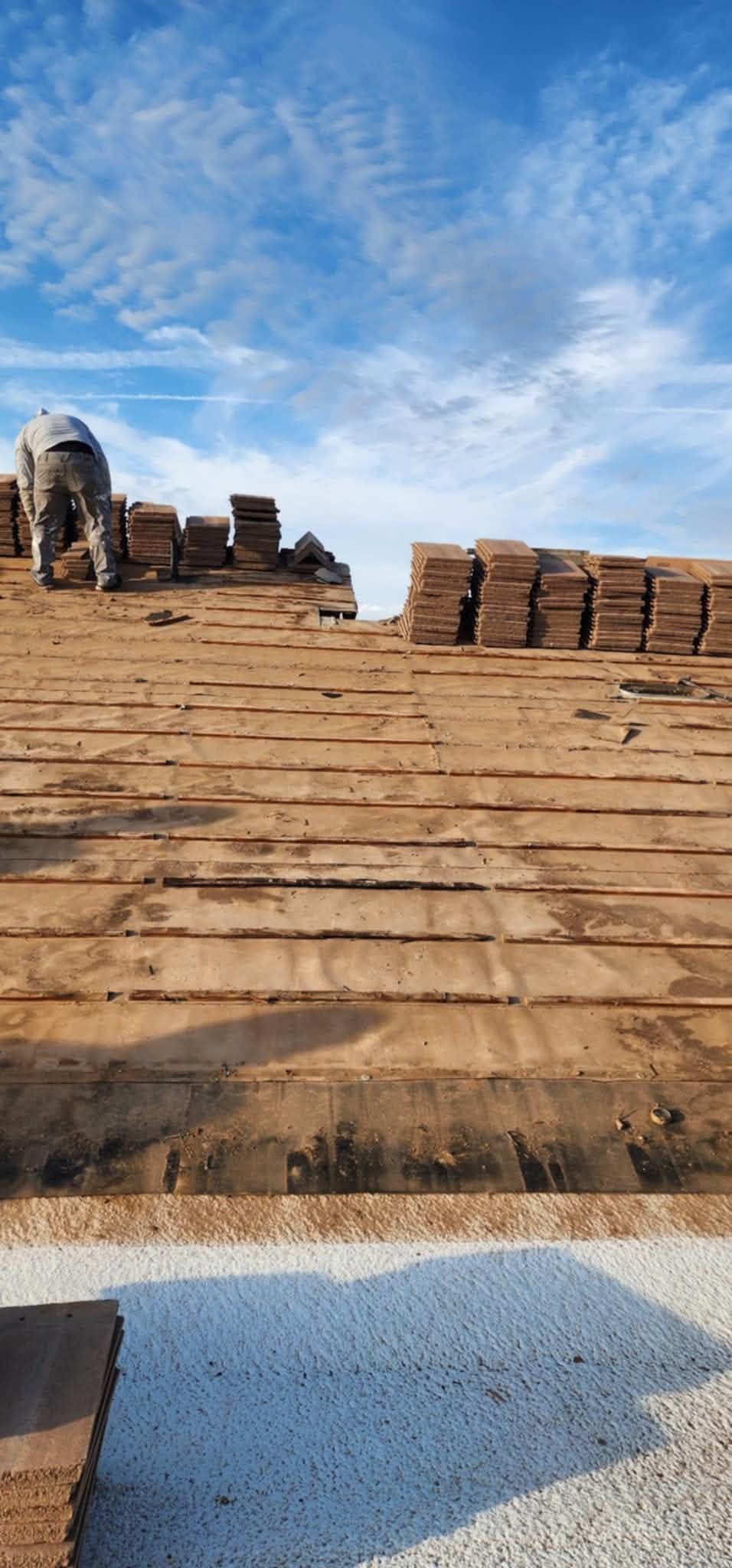Worker on a stepped brick rooftop under a blue, cloud-streaked sky, with stacked bricks nearby