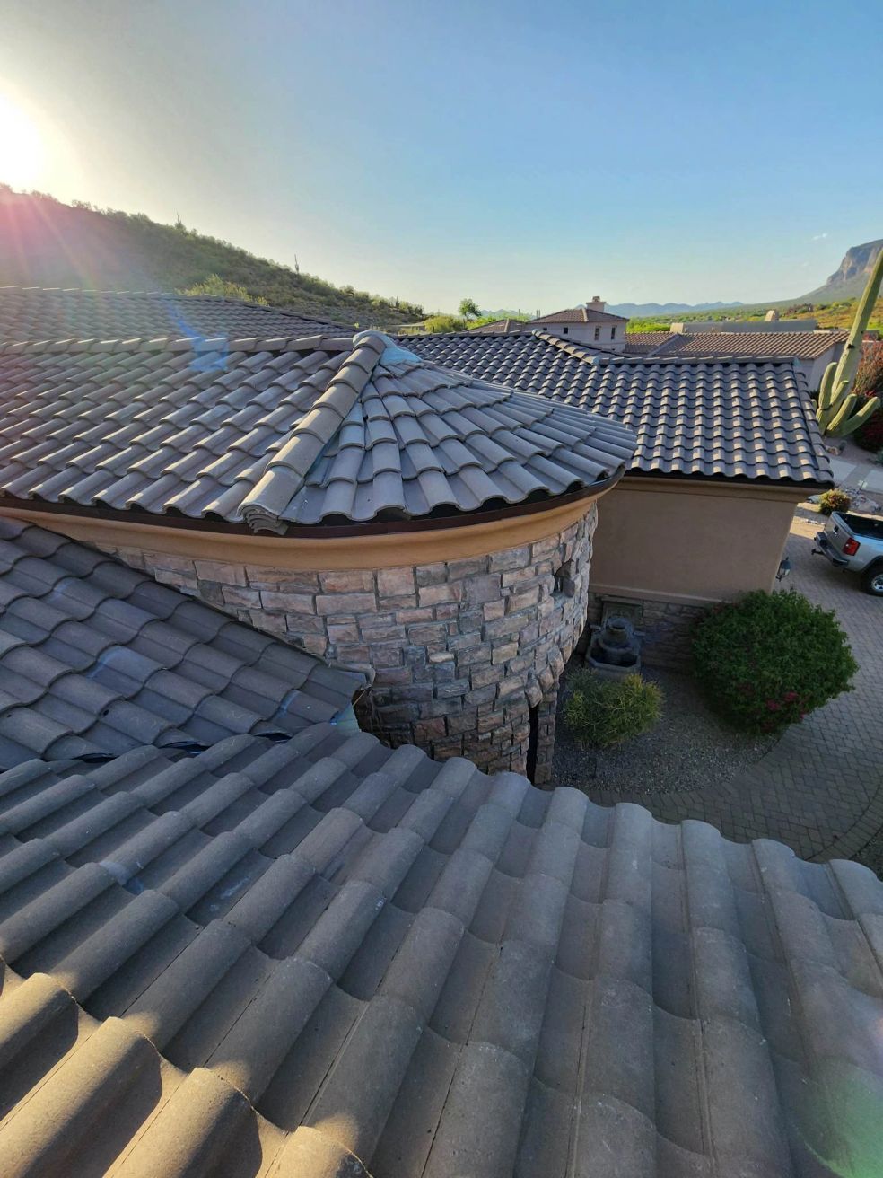 Curved gray tile roofs on a stone house, with a sunlit hillside and blue sky in the background.