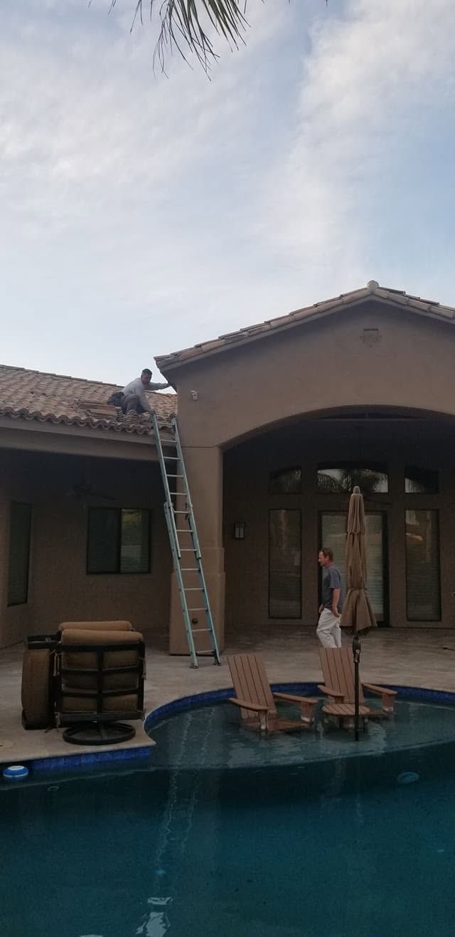 Backyard pool with two people on a small float near a covered patio and ladder against the wall
