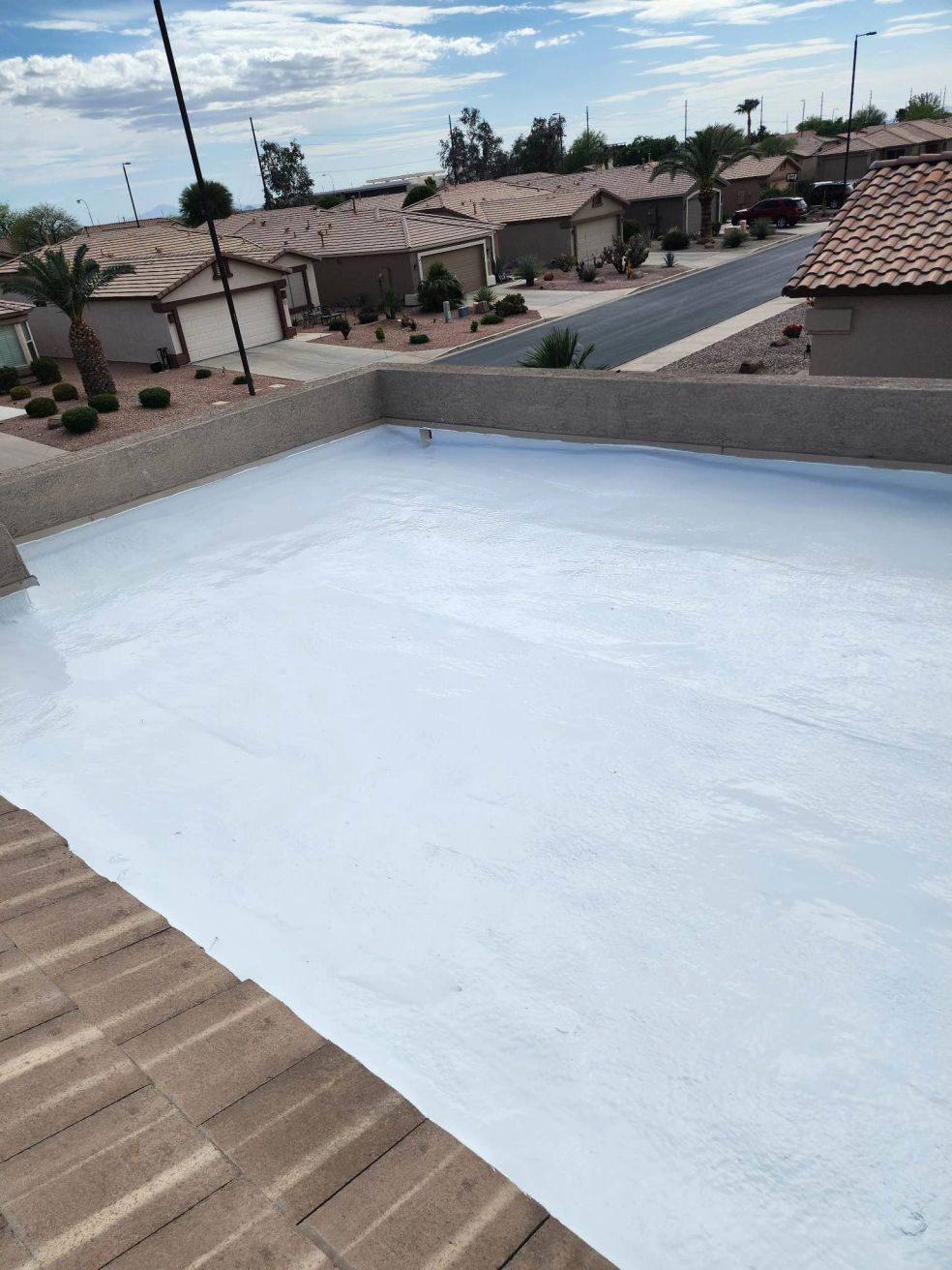 Rooftop with a large white-coated flat section beside terracotta roof tiles, overlooking a suburban neighborhood