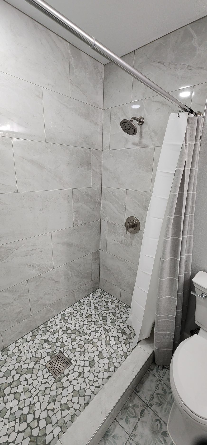 Small tiled shower with bench, grab bars, and a toilet beside it in a bathroom