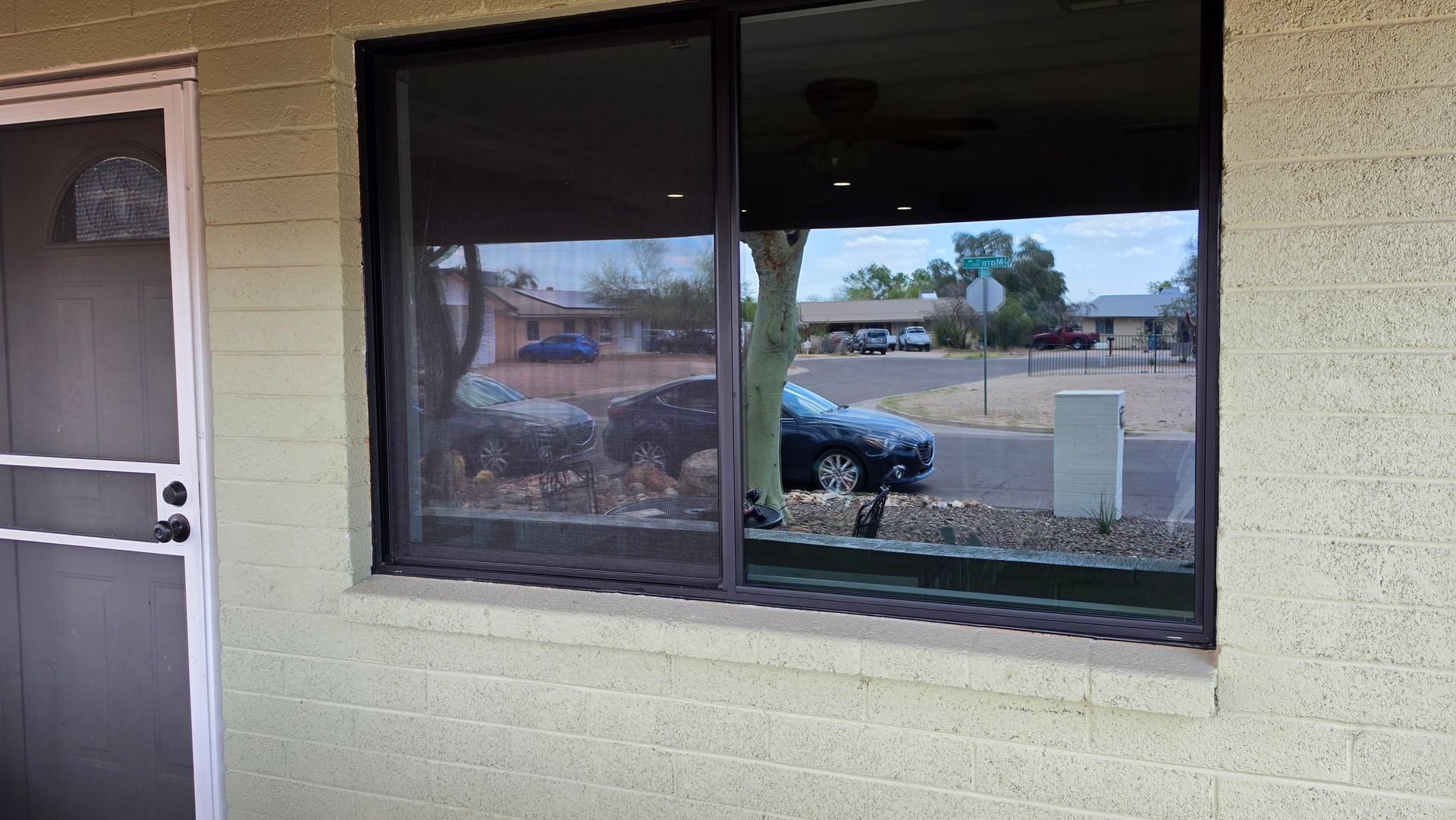Storefront window and door on a beige building, with parked cars and trees reflected in the glass.