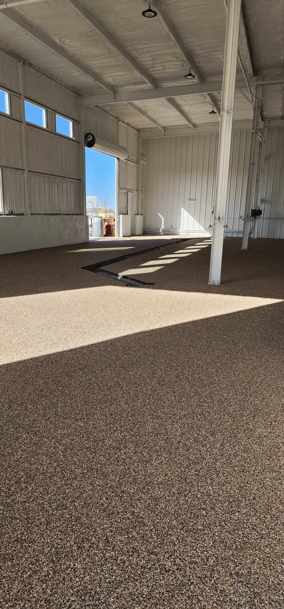 Empty white industrial interior with gravel floor, pillars, and sunlight streaming through an open doorway