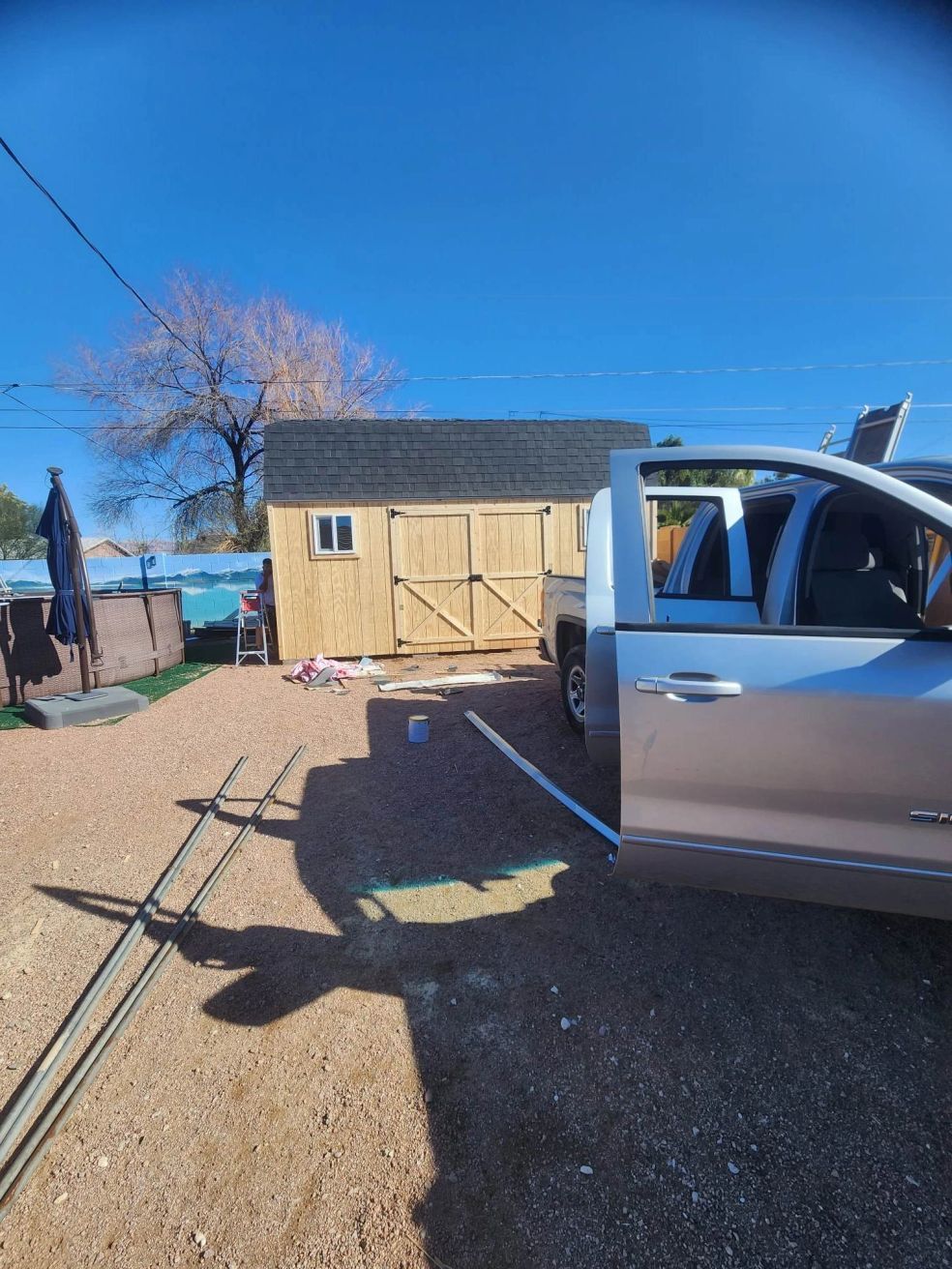 Silver pickup in a gravel yard beside a small shed under a clear blue sky.