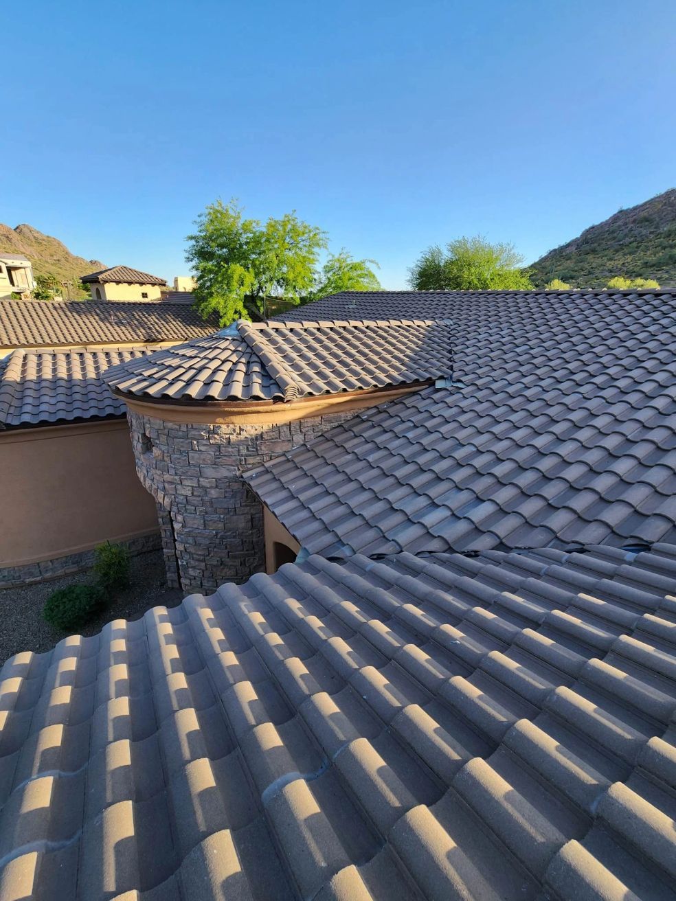 Tile rooftops and stucco homes under a clear blue sky in a hilly residential neighborhood