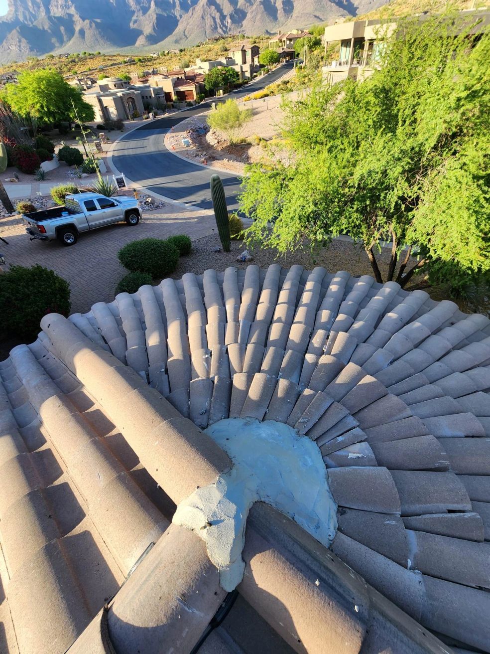 Curved stone rooftop overlooking a desert hillside neighborhood with parked vehicles and green trees
