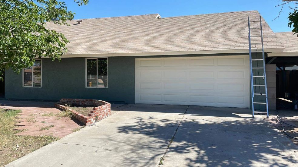 Single-story house with blue siding, white garage door, concrete driveway, and a ladder by the roofline