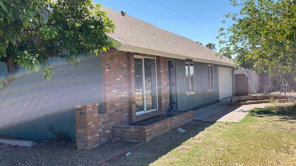 Single-story brick house with front windows, a driveway, and a sunny front yard.