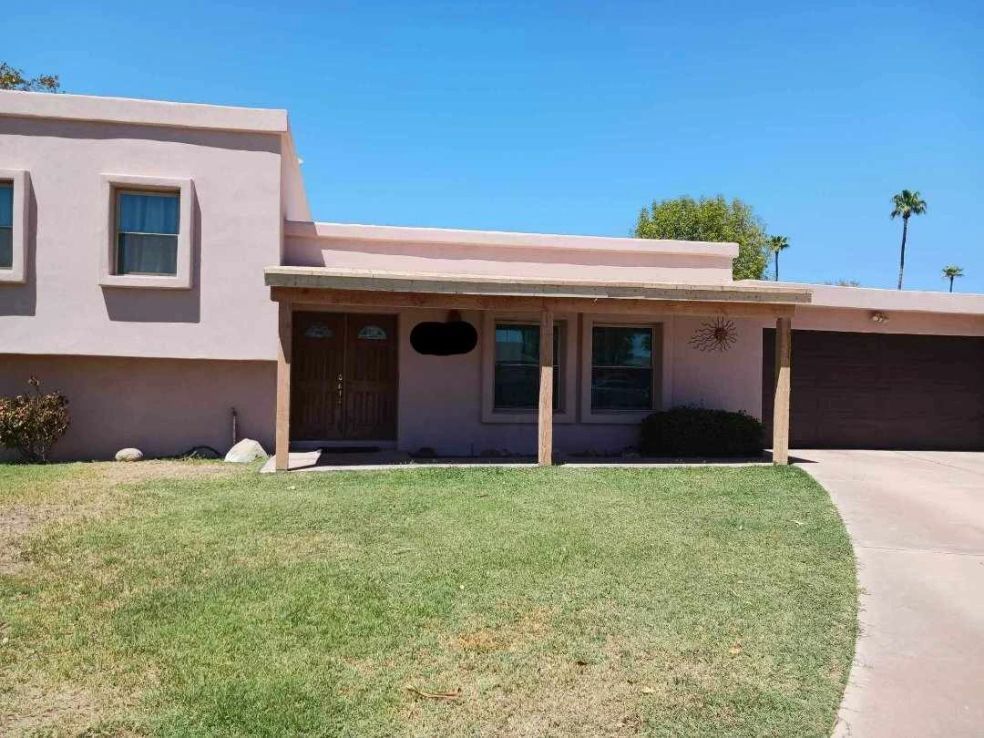 Single-story house with beige stucco exterior, front lawn, and driveway under a clear blue sky