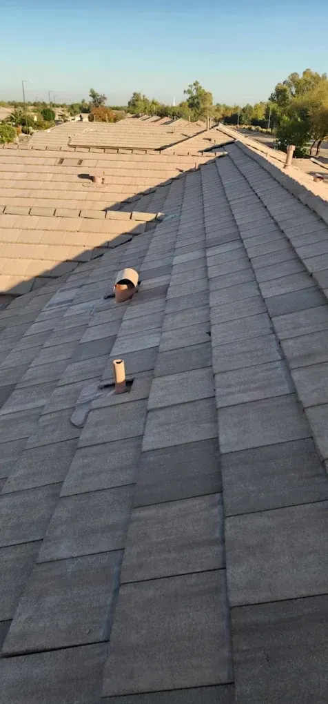 Roof covered in gray shingles with a small vent, viewed along the ridge in daylight