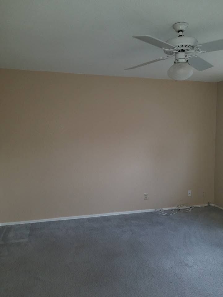 Empty beige room with gray carpet and a white ceiling fan overhead