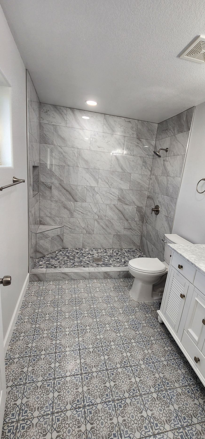 Modern marble bathroom with patterned tile floor, toilet, and white vanity under recessed lights