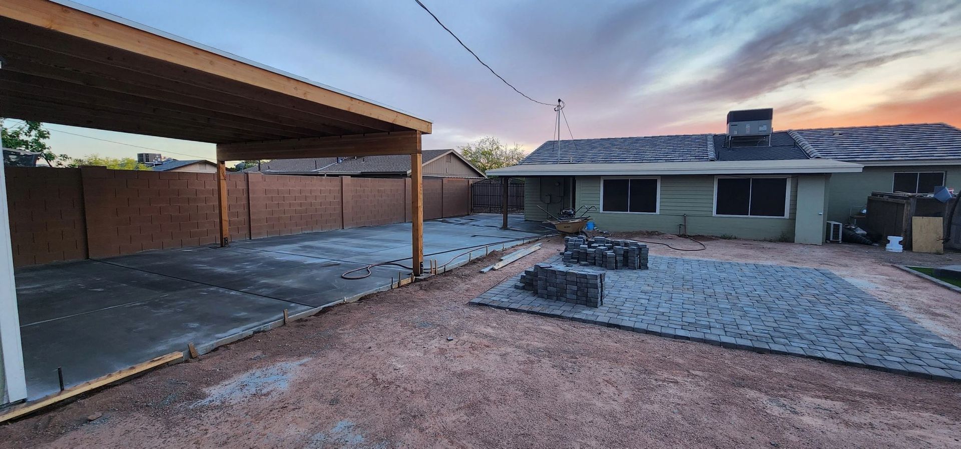 Backyard with a covered carport, gravel yard, and single-story house at sunset