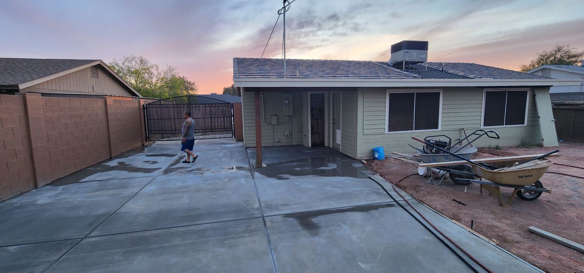 Driveway and single-story house exterior with scattered yard debris at dusk