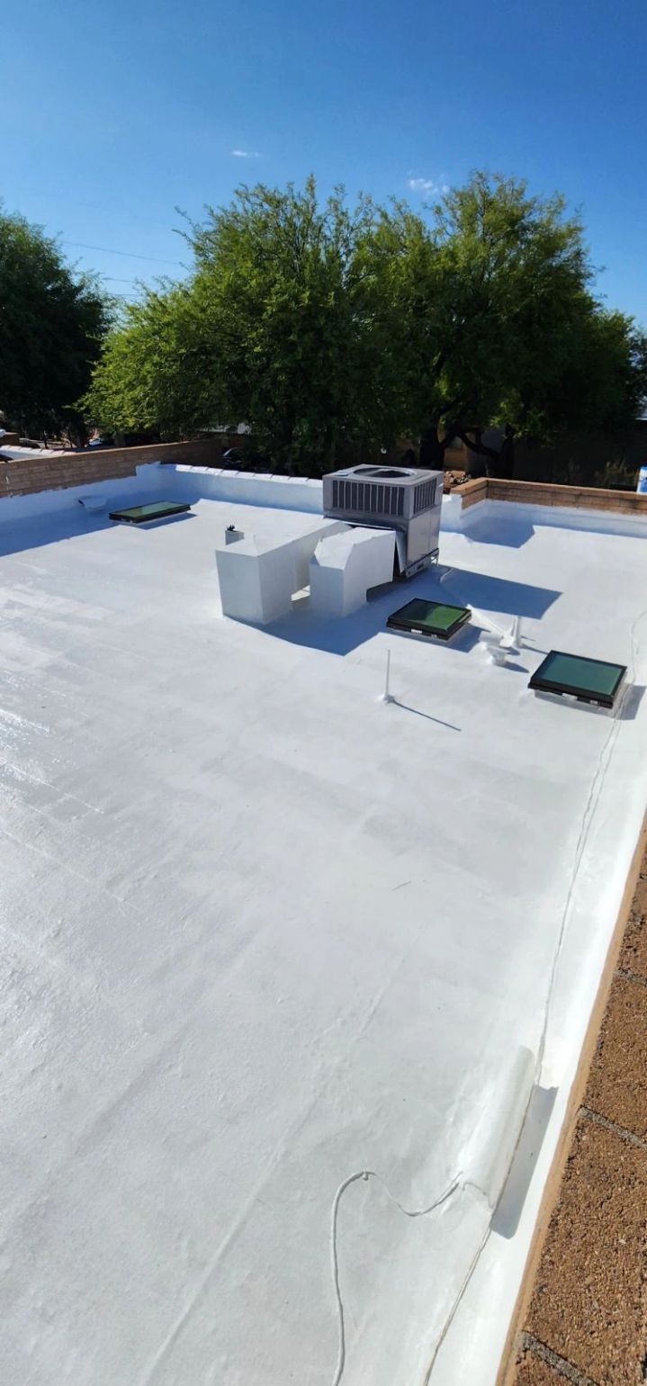 Flat white rooftop with HVAC units and vents under a clear blue sky, trees in the background