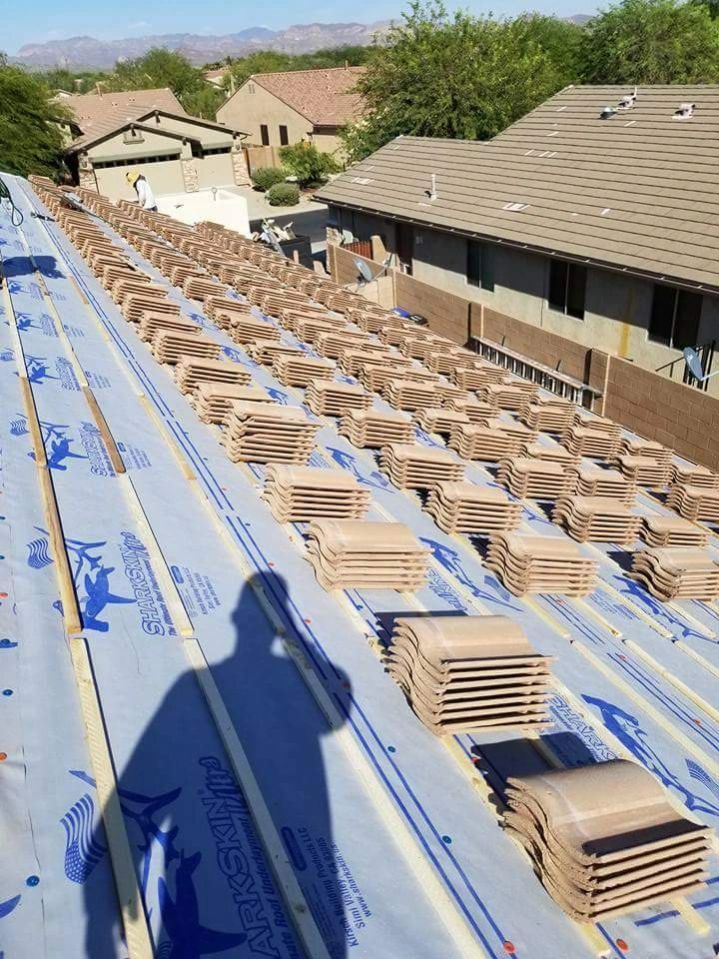 Roof under construction with rows of stacked shingles on blue underlayment in a suburban neighborhood