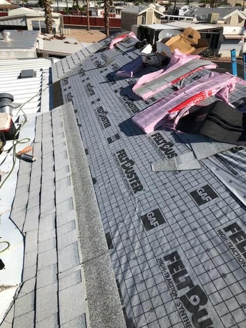 Roof under construction with gray underlayment and pink insulation on a sloped rooftop