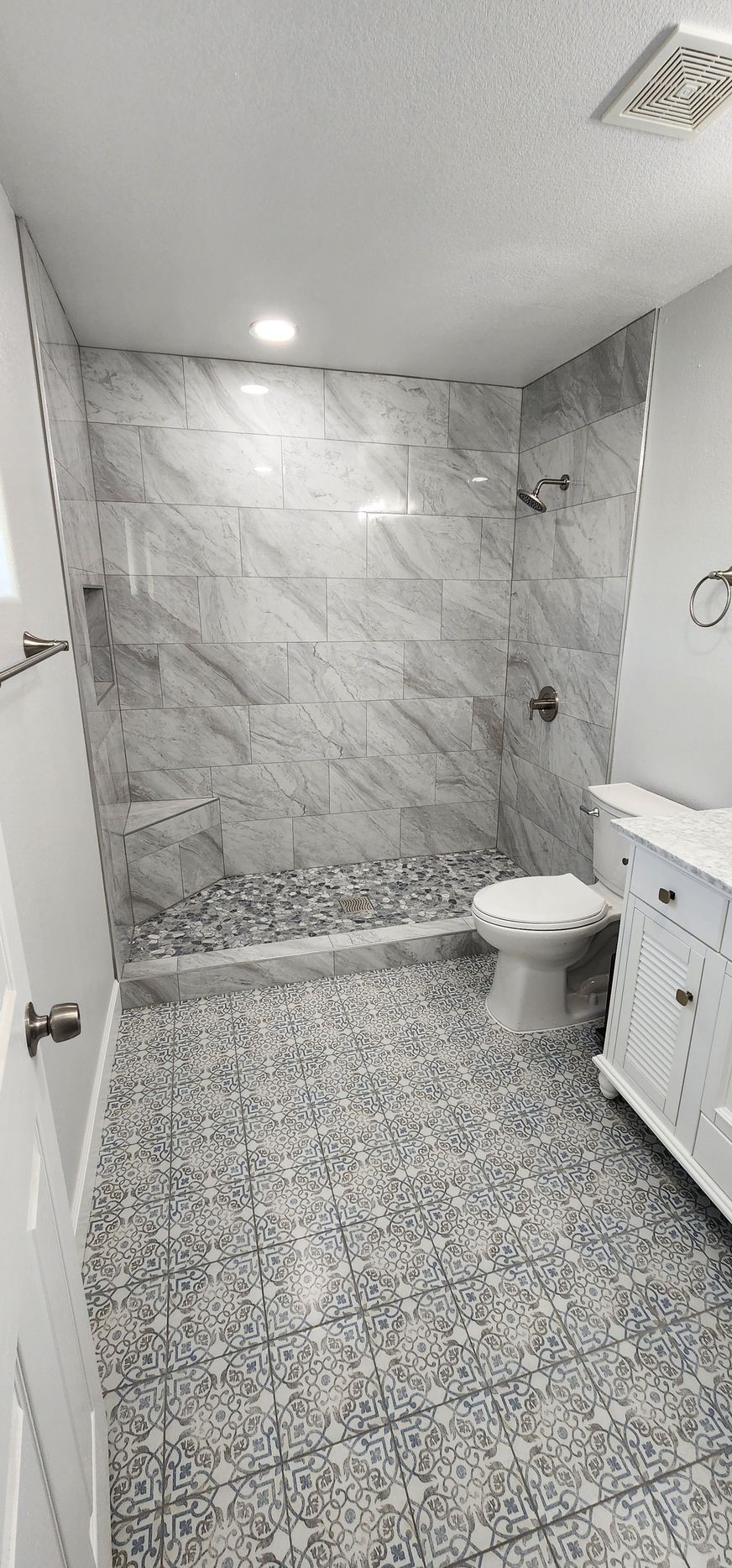 Small tiled bathroom with marble-look walls, patterned floor, toilet, and white vanity.