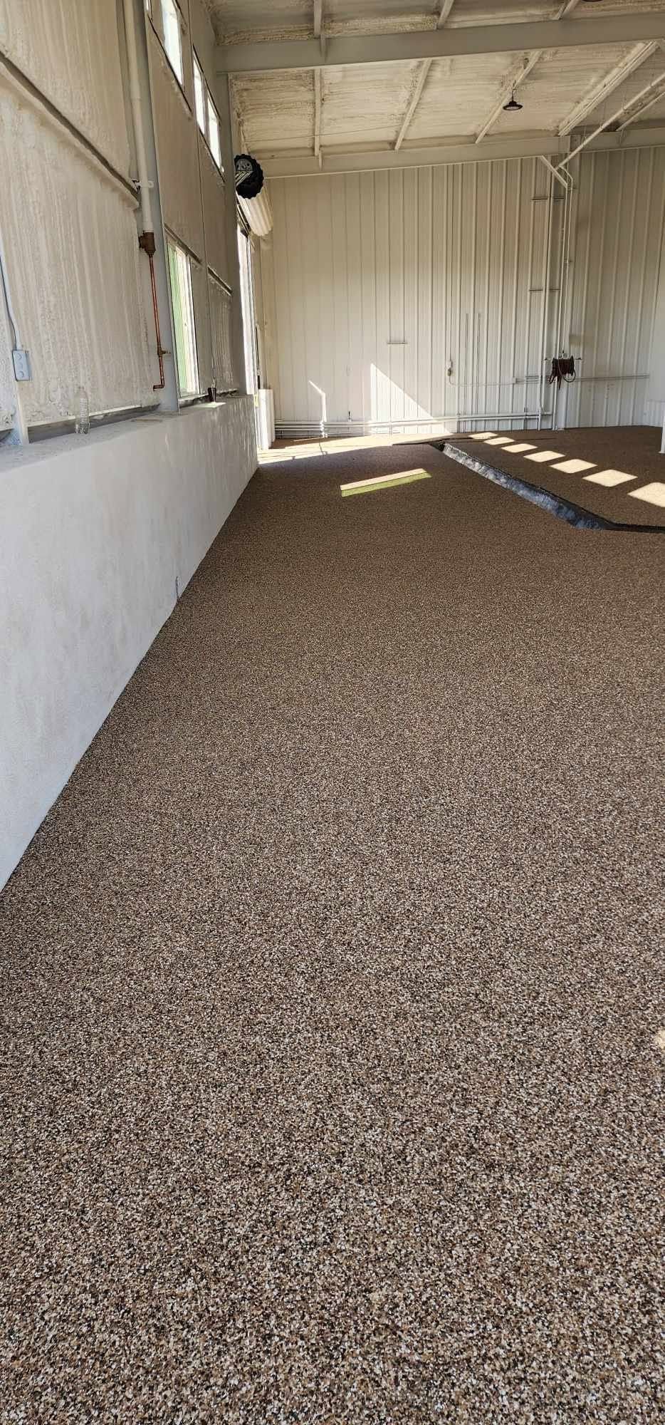 Empty covered porch with gravel floor, white walls, and sunlight streaming in through the open side