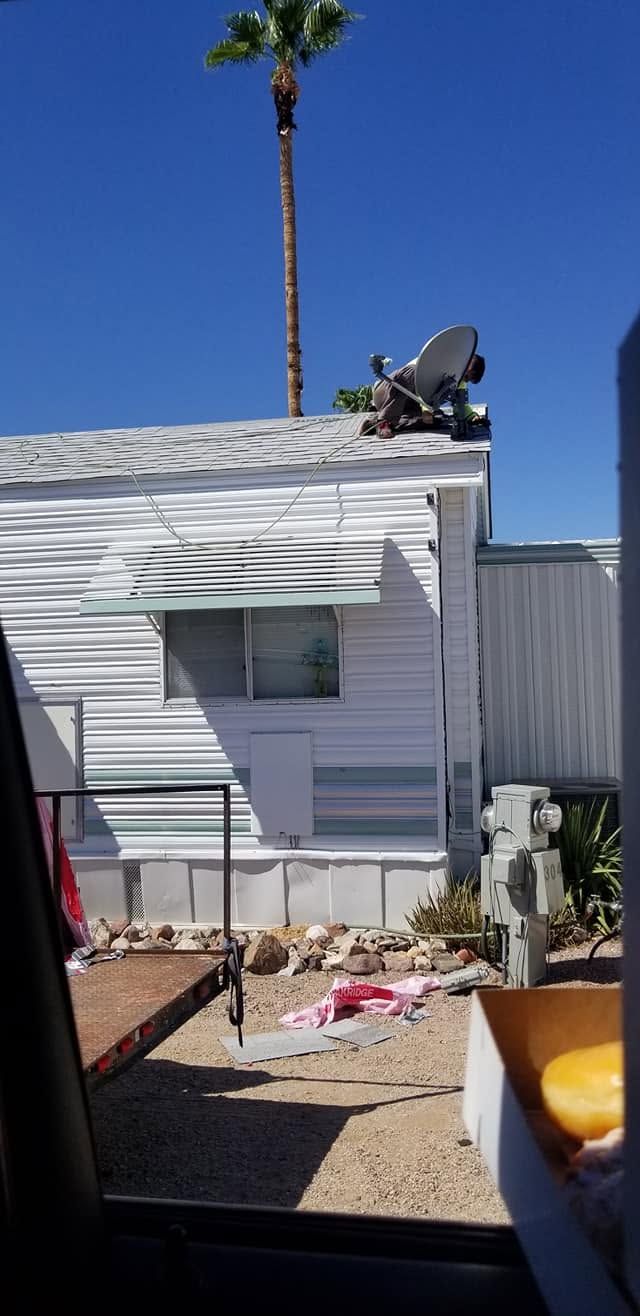 Mobile home exterior with a rooftop satellite dish, blue sky, and a palm tree behind it
