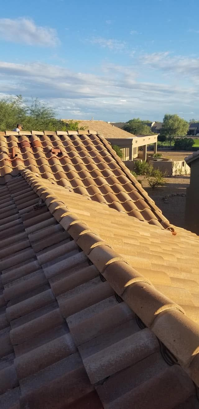 Tile rooftops under a blue sky, with a tan roof in the foreground and a building in the distance
