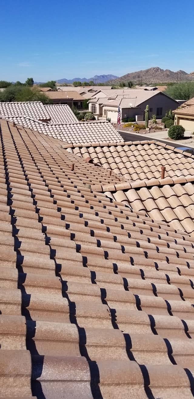Desert neighborhood rooftops with tan tile shingles, houses, and mountains in the distance under clear sky