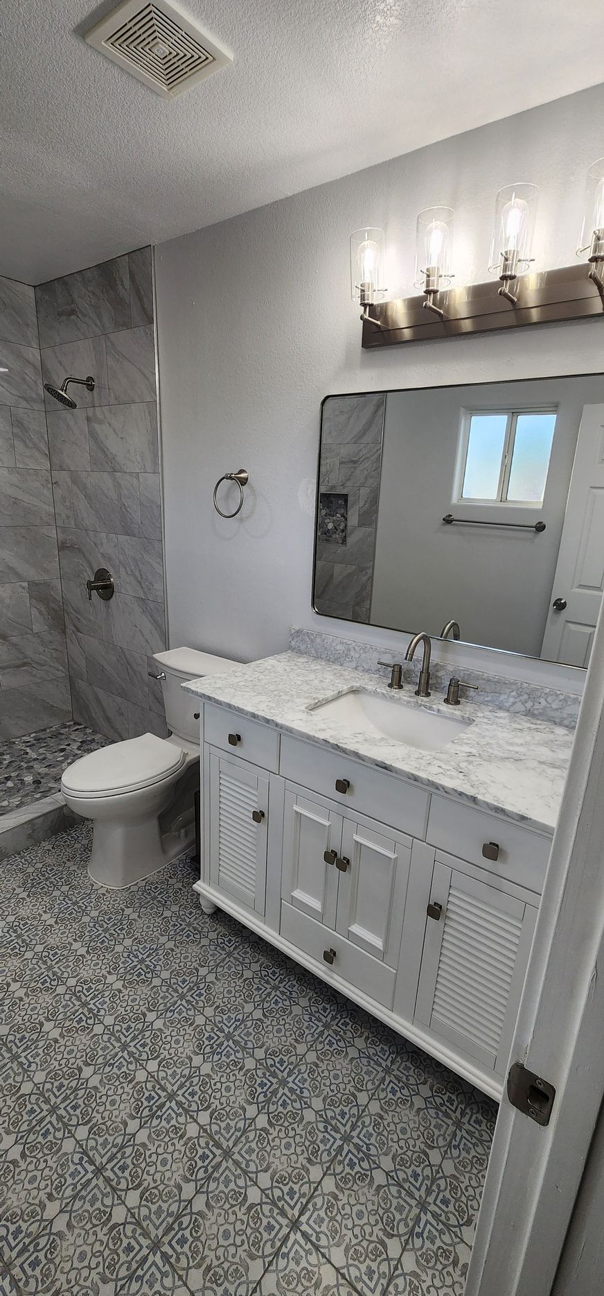 Gray marble bathroom with toilet, vanity sink, large mirror, and patterned floor tile