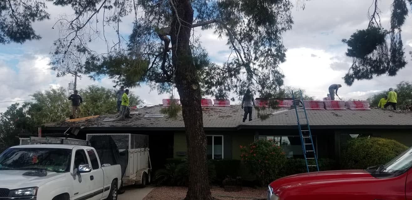 Single-story house under tall trees with a white truck parked left and red car parked right