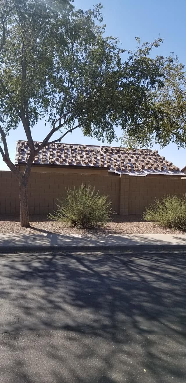 Single-story house with a tiled roof, trees, and desert landscaping in bright sunlight.