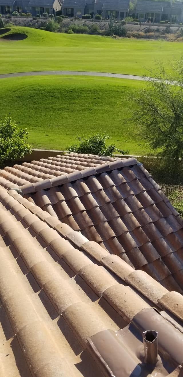 Rooftop terracotta tiles overlooking a bright green field and distant trees under clear daylight