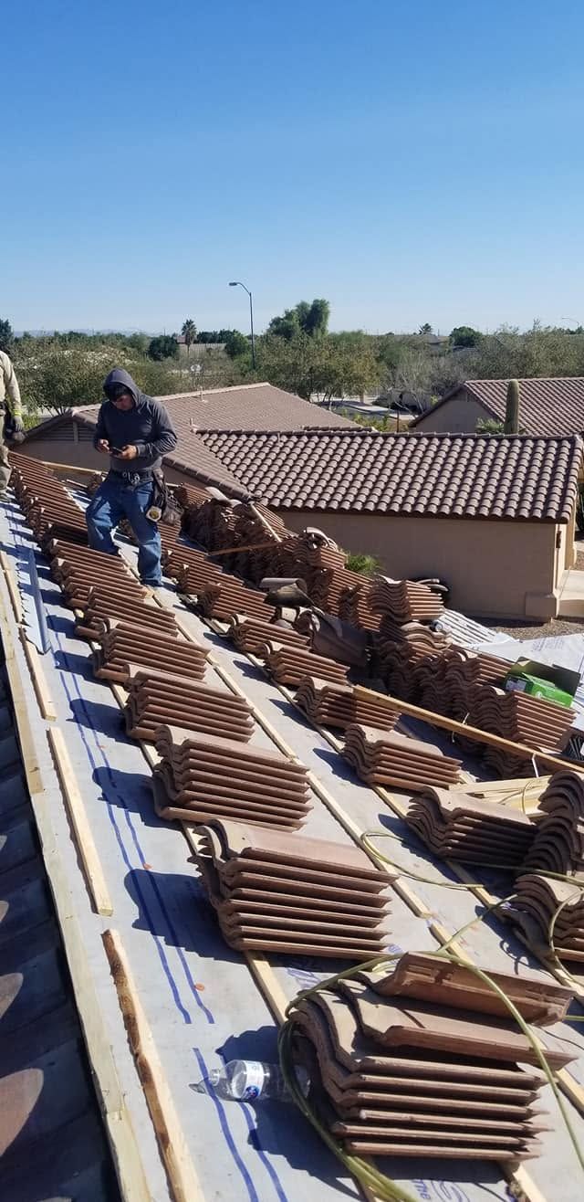 Roofers installing terracotta tiles on a sloped rooftop under a blue sky